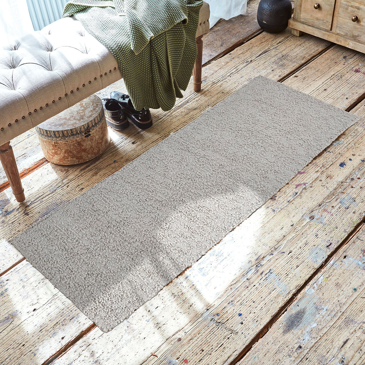 Tapis Kaleema Tapis gris en tissu doux sur un sol en bois dans un intérieur chaleureux avec banc et couverture verte
