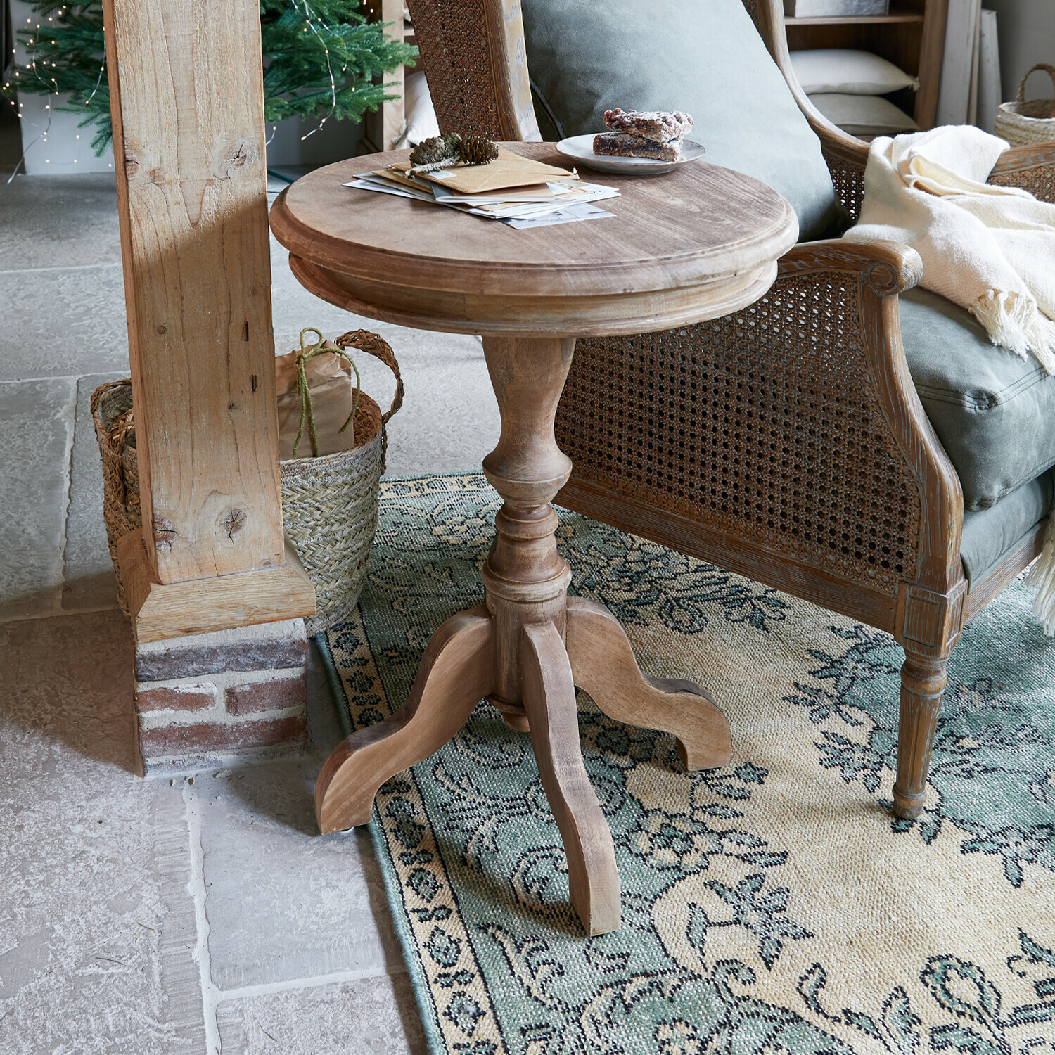 Table d’appoint Mengomeyen Table ronde en bois naturel à côté d'un fauteuil en osier sur un tapis à motifs