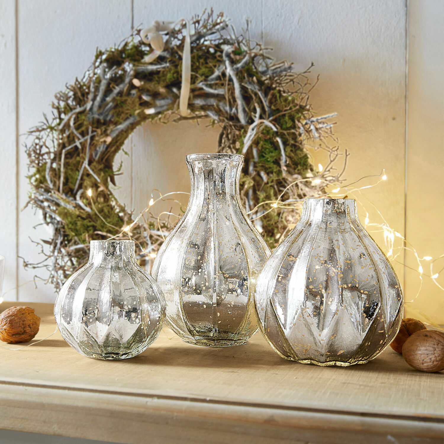 Lot de 3 vases Frido Ensemble de trois vases décoratifs en verre argenté sur une table en bois avec une couronne naturelle en arrière-plan