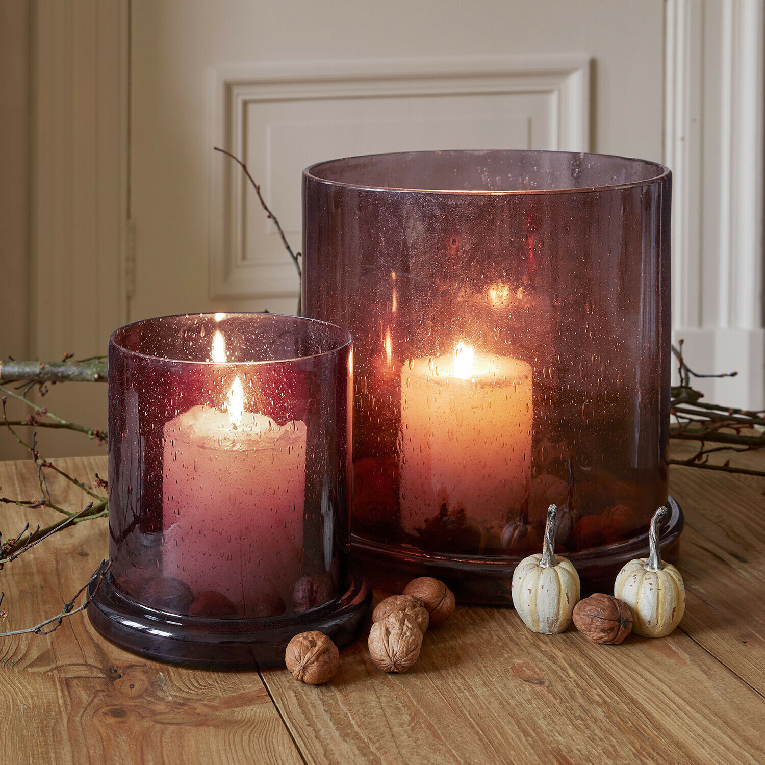 Lot de 2 photophores Saffrone Deux bougies allumées dans des photophores en verre violet sur une table en bois avec décorations d'automne
