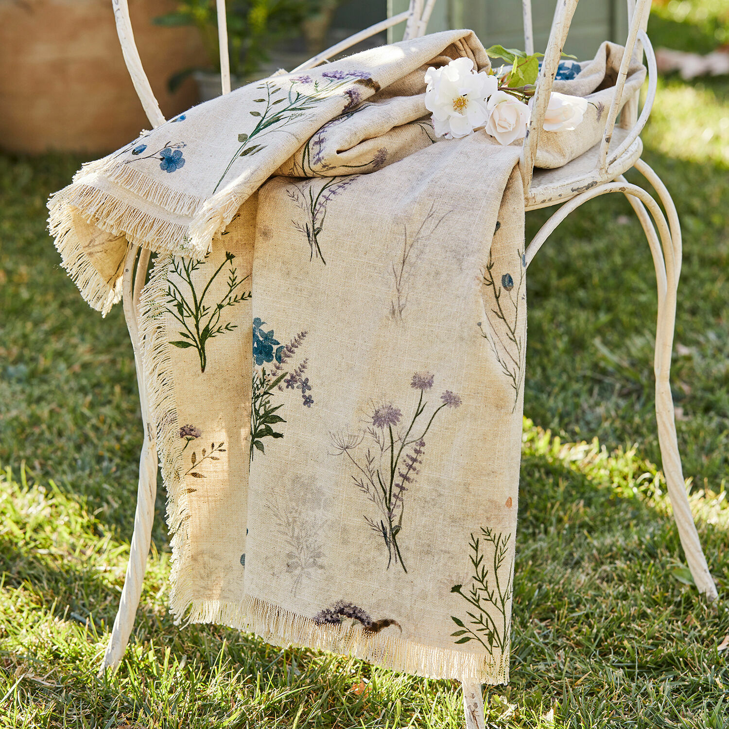 Plaid Cabinda Nappe en lin beige avec imprimé floral et franges sur chaise en métal blanc dans un jardin