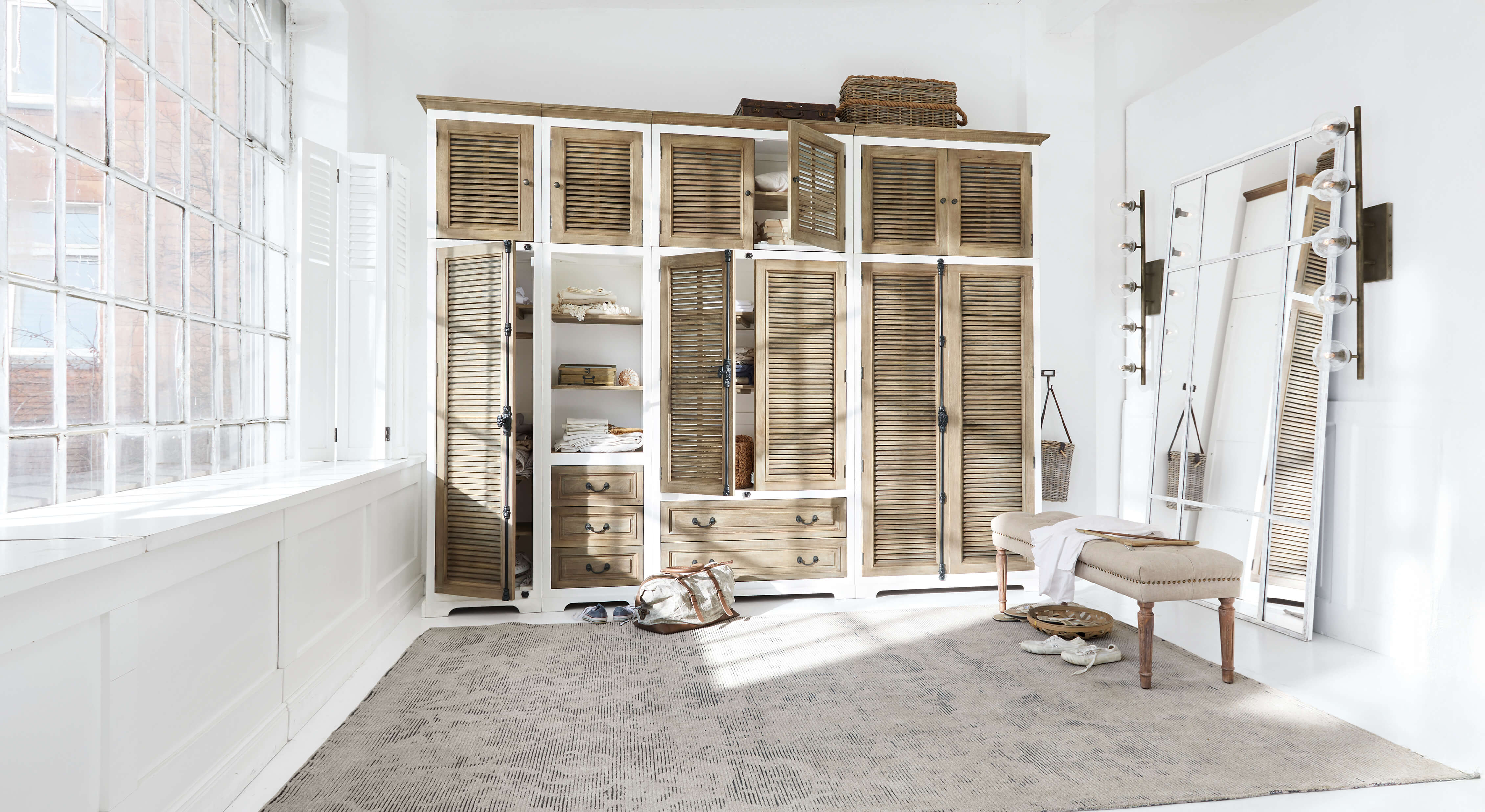 Grande armoire en bois blanc et naturel avec portes à persiennes et grand miroir dans une pièce lumineuse