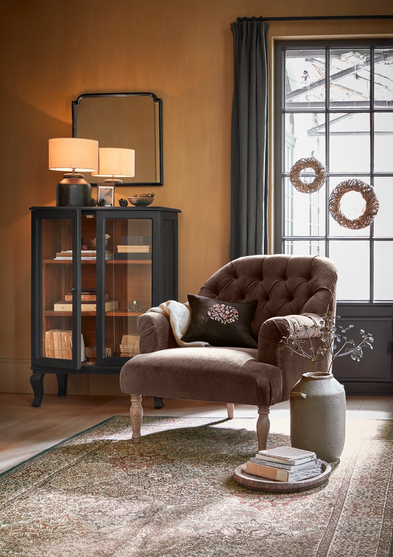 Fauteuil en velours marron avec dossier capitonné dans un salon chaleureux avec vitrine noire et lampe