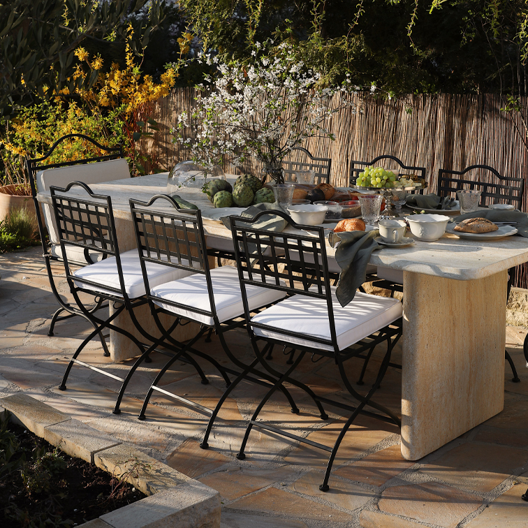 Ensemble de jardin avec chaises en métal noir et table en pierre claire sur terrasse avec décorations et repas