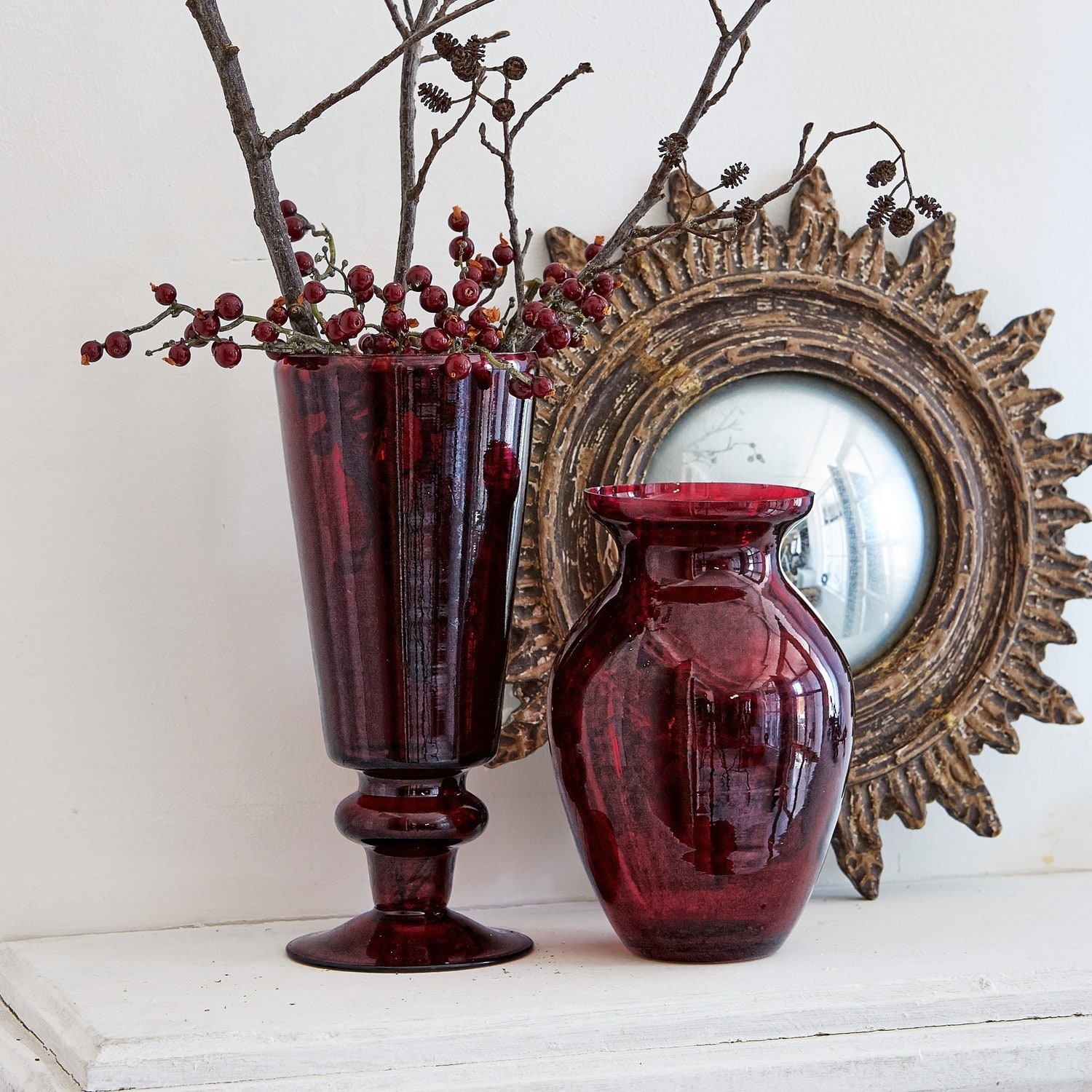 Lot de 2 vases Darian Deux vases en verre rouge posés sur une surface blanche avec un miroir décoratif en arrière-plan