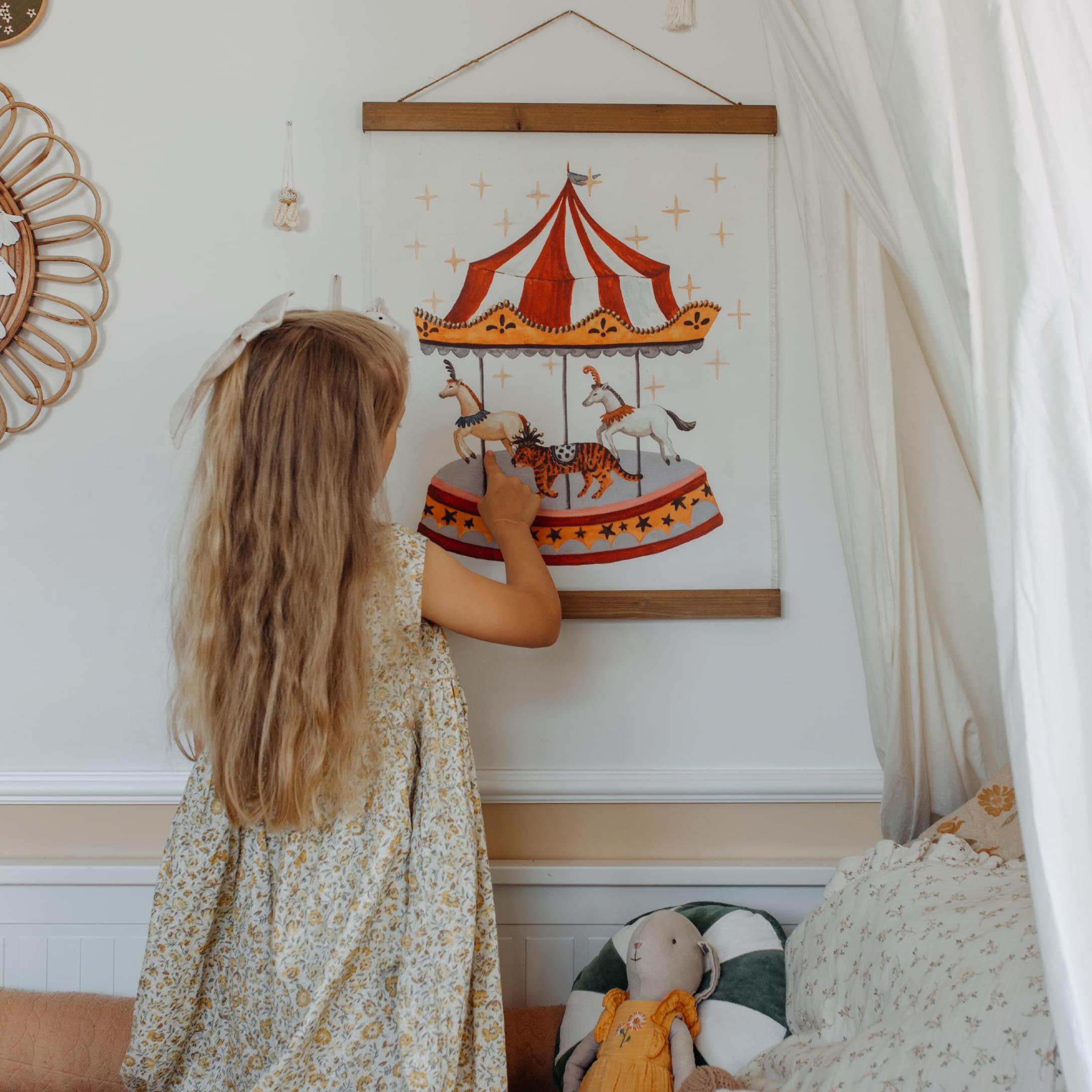 Petite fille touche une illustration de manège avec chevaux et tigre dans une chambre d'enfant décorée
