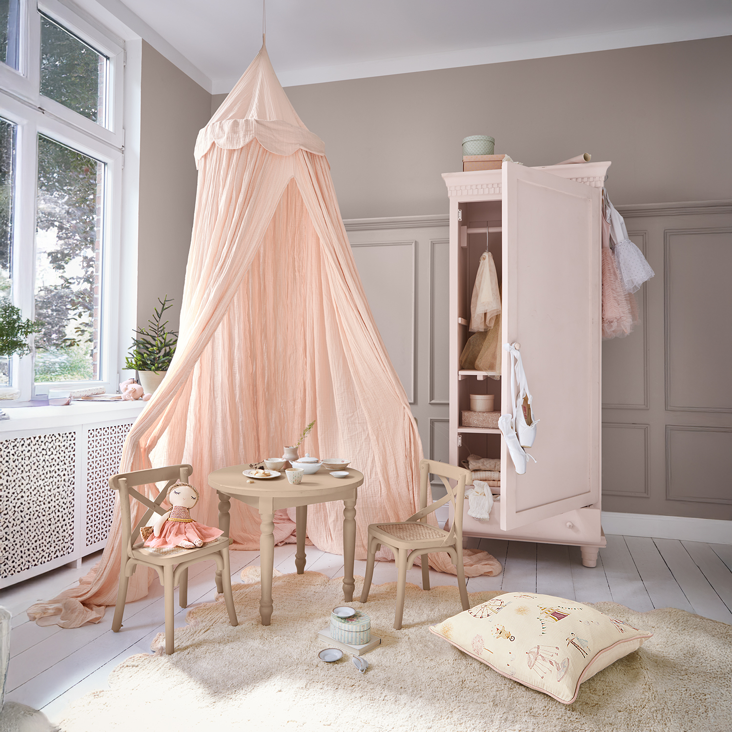 Chambre d'enfant douce avec baldaquin rose, table et chaises en bois, armoire rose ouverte avec vêtements