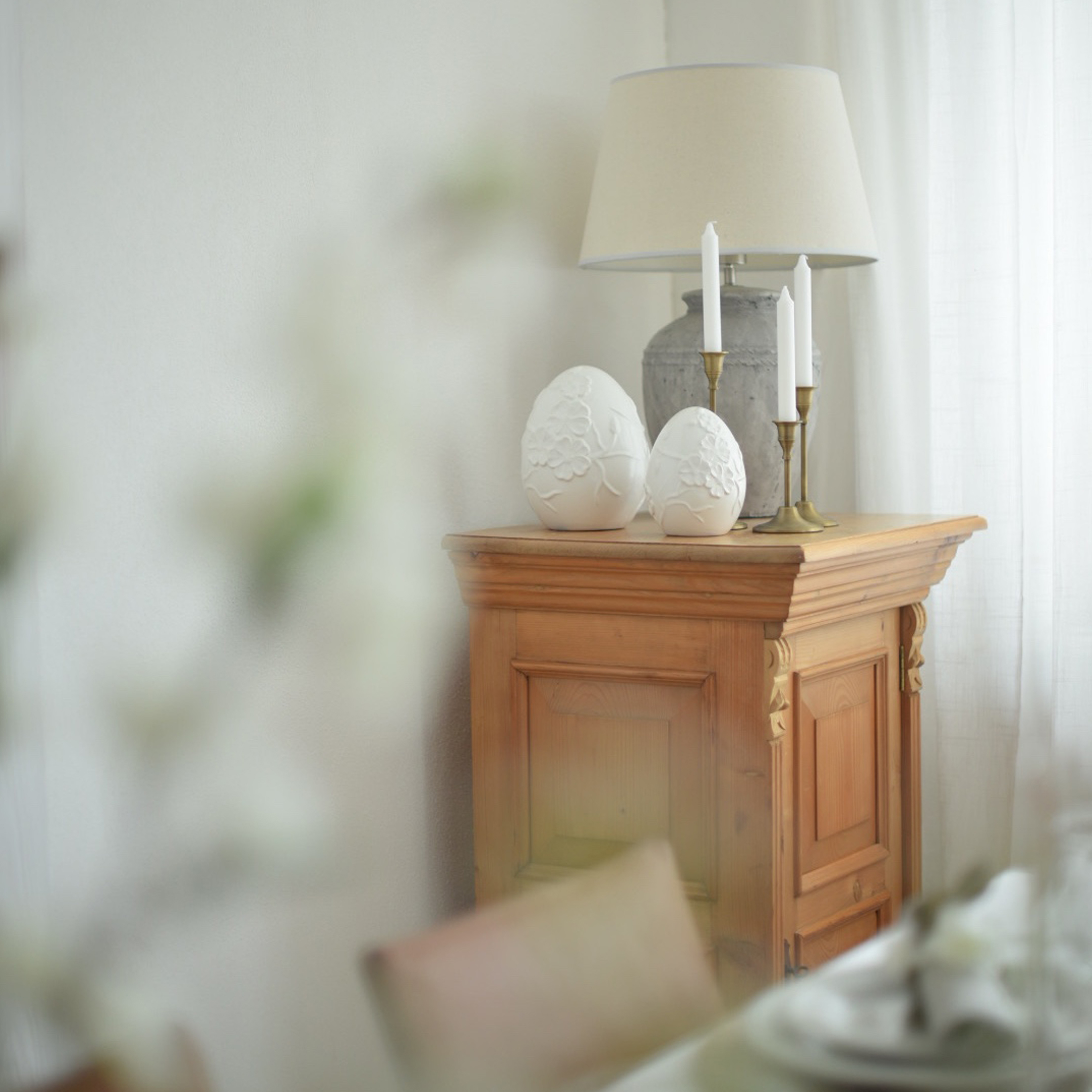 Meuble en bois avec lampe, bougies et décorations en céramique blanche en forme d'œufs dans un intérieur lumineux