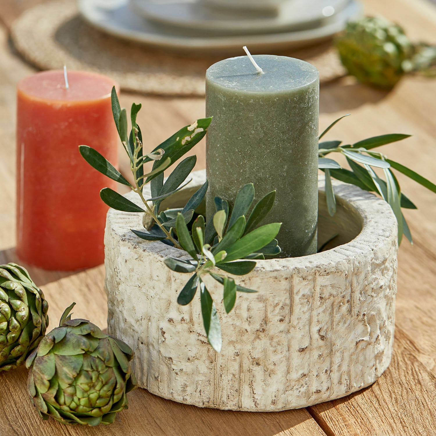 Coupe Continas Bougeoir rond en pierre beige avec une bougie verte et décoration de feuilles sur une table en bois