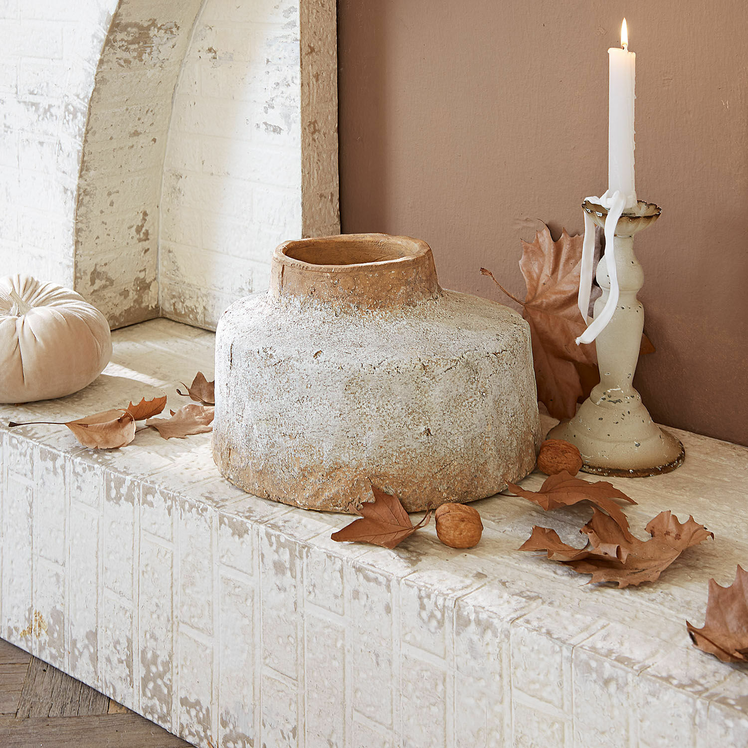 Vase Sévrac Vase décoratif en céramique beige posé sur un rebord en pierre avec feuilles d'automne et bougie allumée