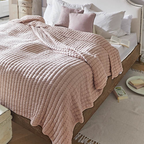 Plaid matelassé rose sur lit en bois avec coussins blancs dans une chambre chaleureuse