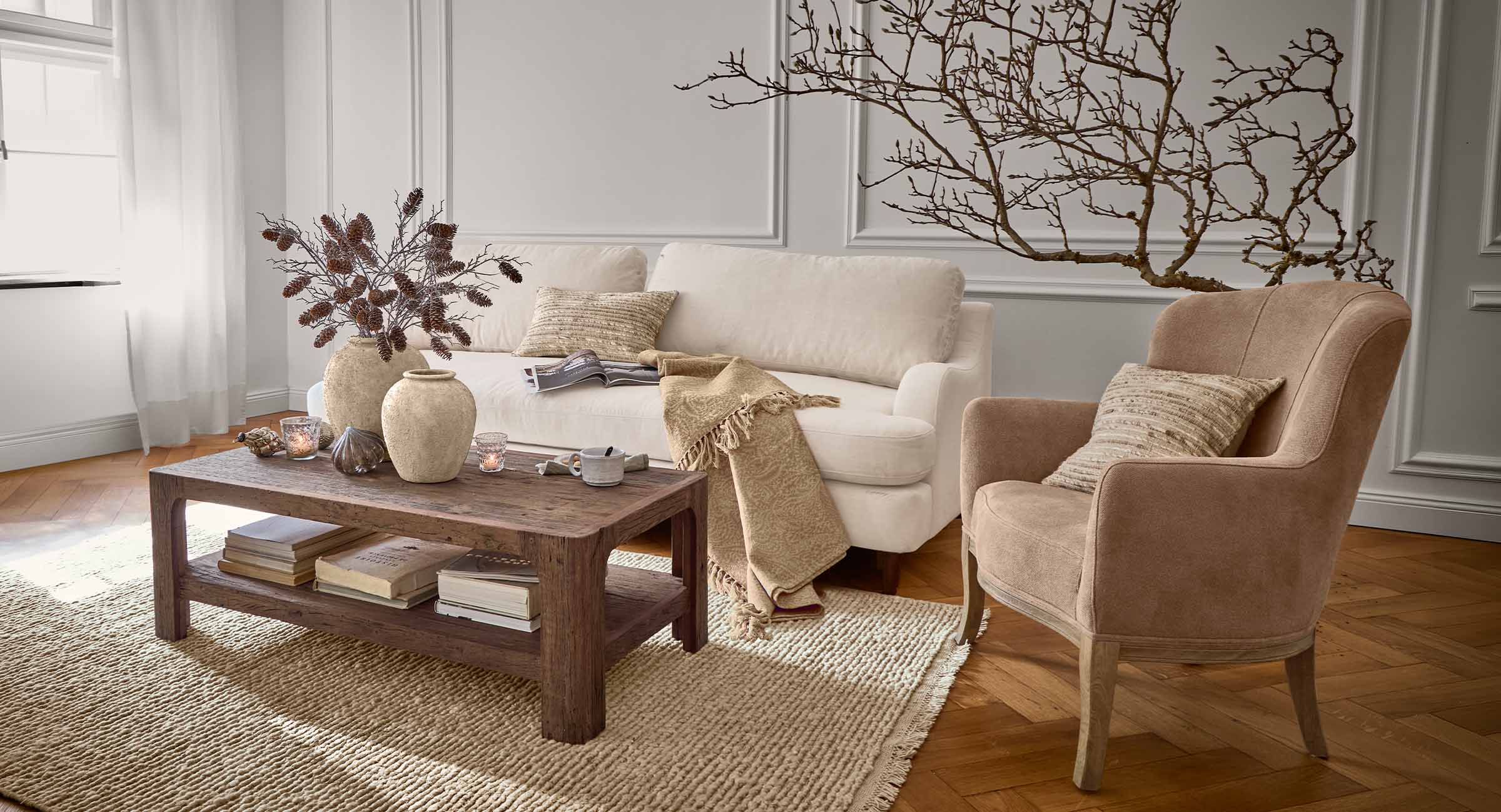 Salon chaleureux avec canapé beige, fauteuil marron et table basse en bois sur tapis en fibres naturelles