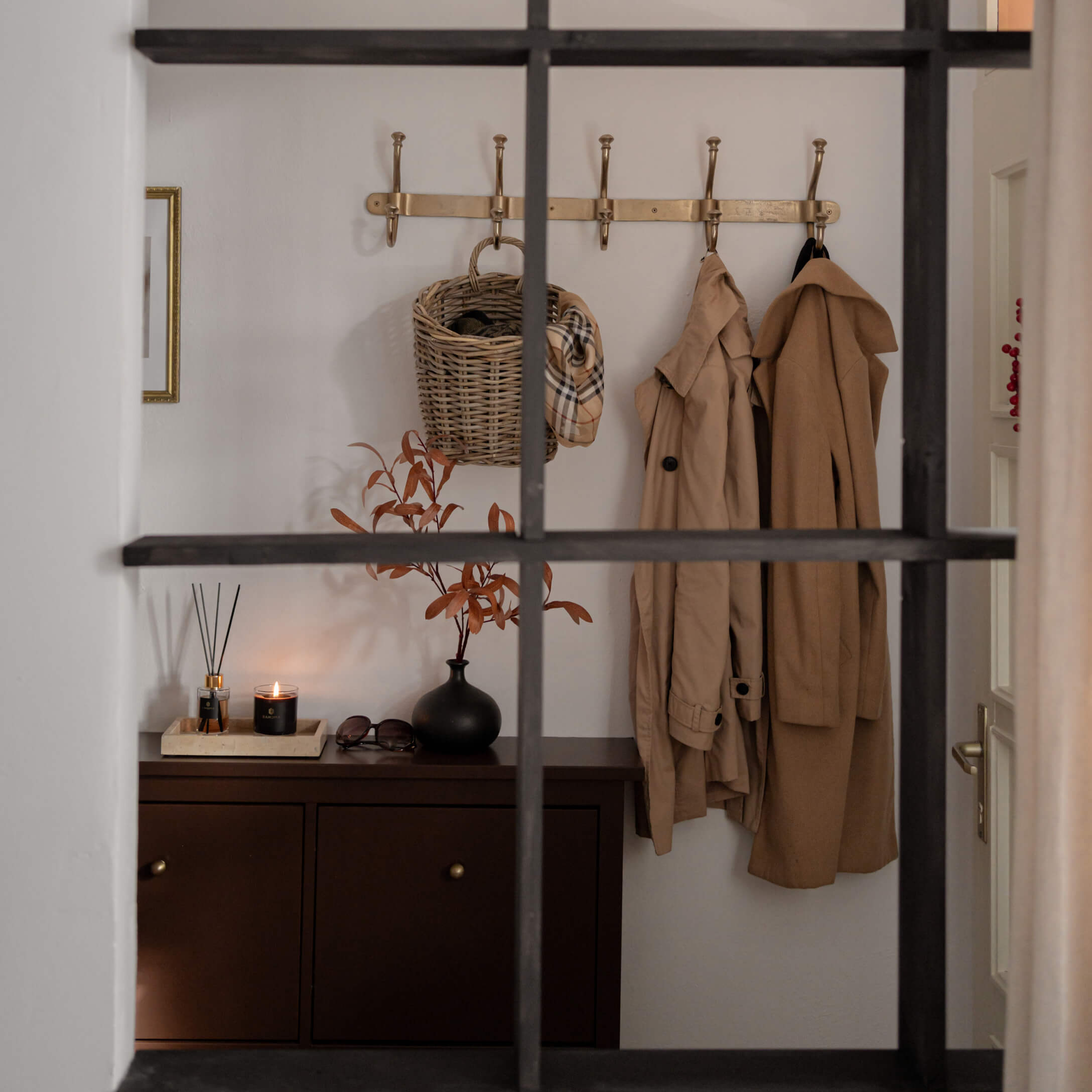 Entrée avec meuble marron, manteaux beige et panier en osier sur patère dorée