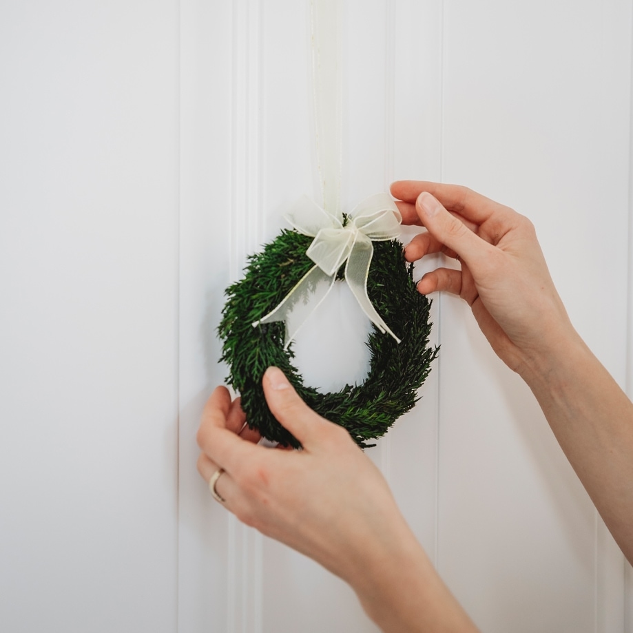 Petit couronne de Noël verte avec un nœud blanc suspendue à une porte blanche, décoration festive