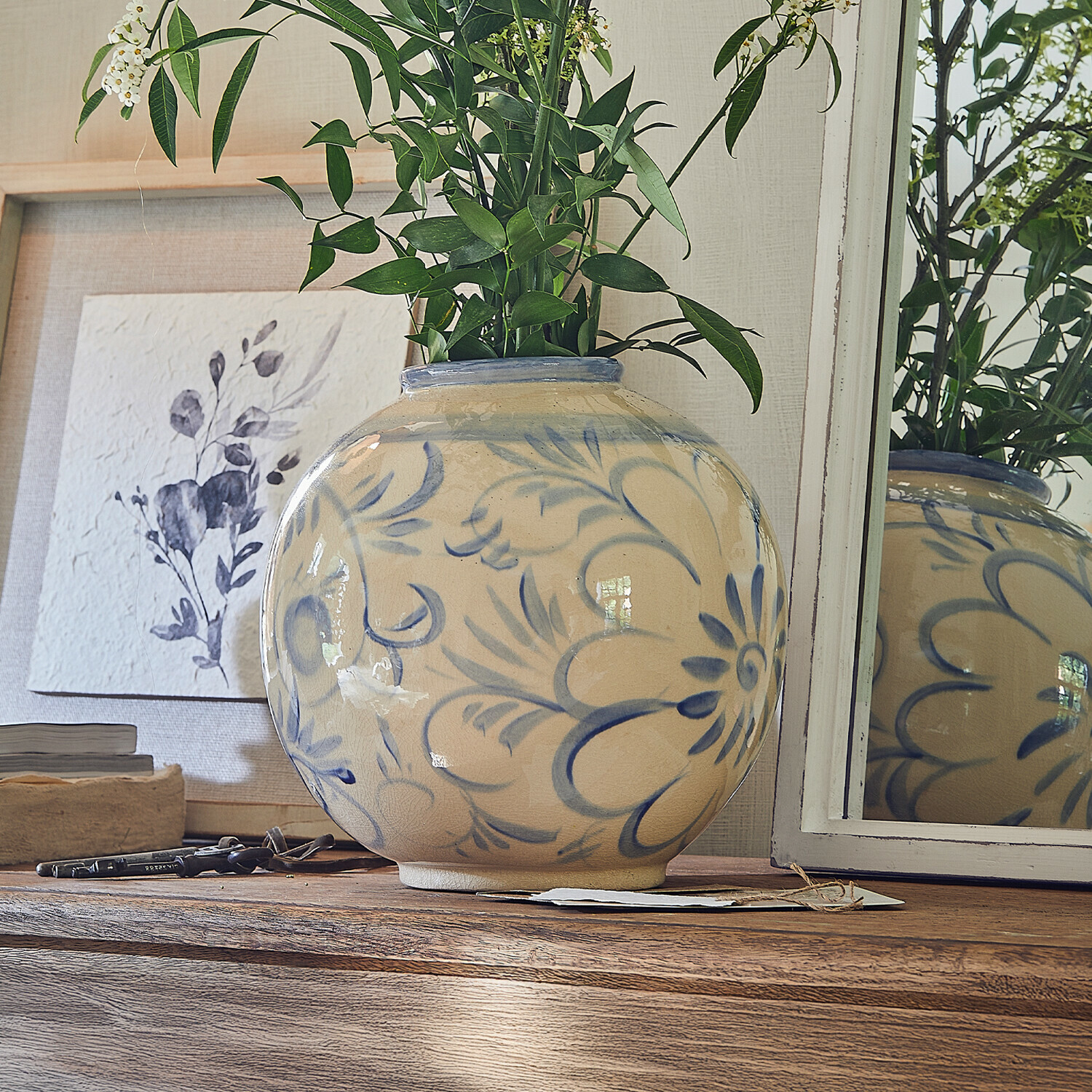 Vase Oviren Vase rond en céramique beige avec motif floral bleu sur table en bois avec feuillage vert