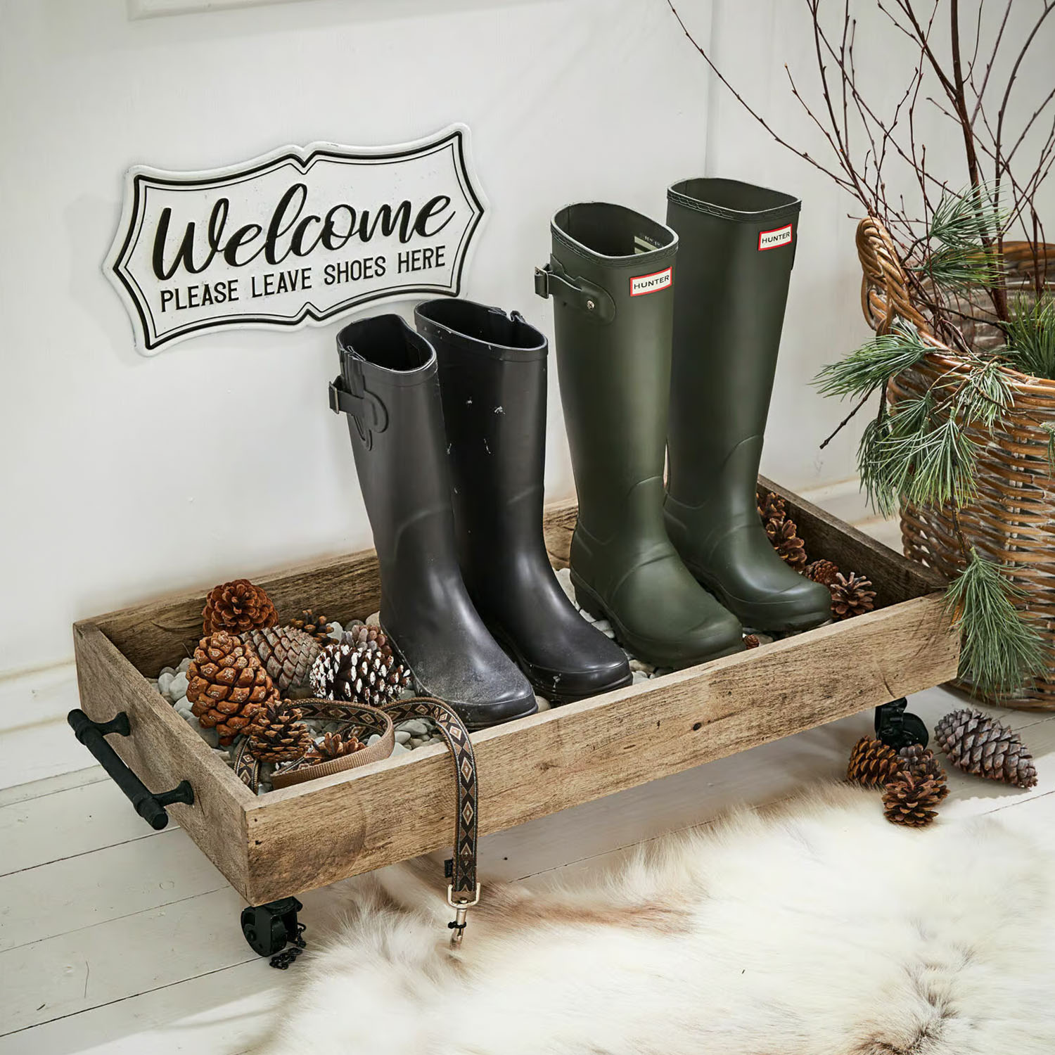 Plateau en bois sur roulettes avec bottes noires et vertes et pommes de pin dans un intérieur chaleureux