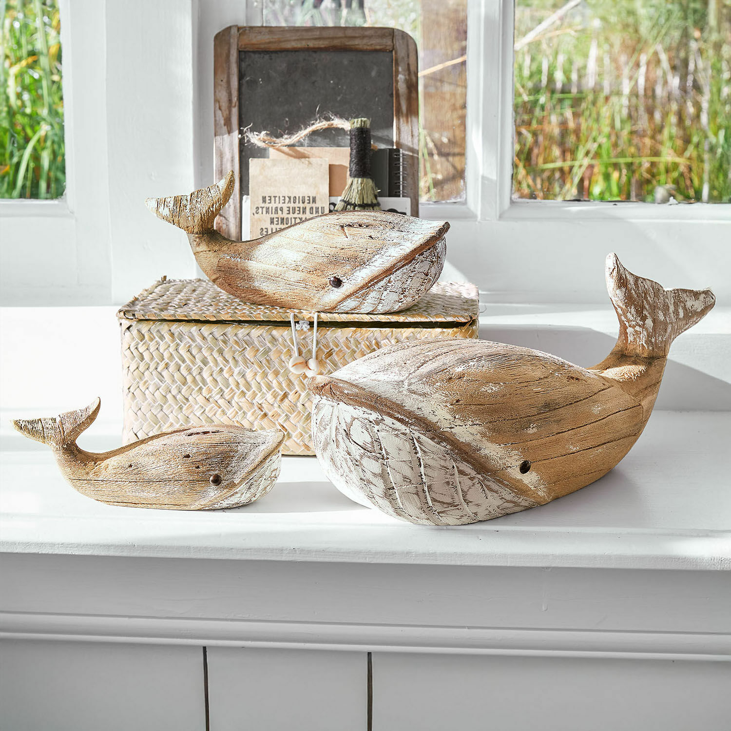 Lot de 3 baleines décoratives Breezie Ensemble de trois baleines décoratives en bois naturel avec accents blancs posées sur un rebord de fenêtre