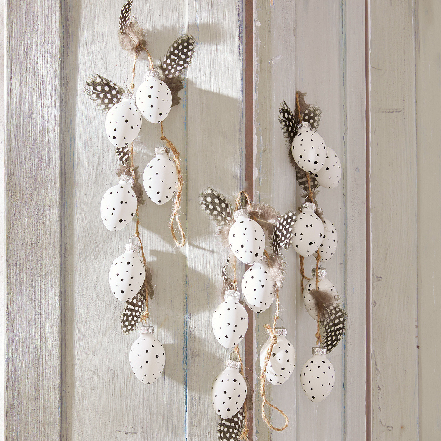 Lot de 3 guirlandes Prina Guirlande décorative avec œufs blancs à pois noirs et plumes sur fond bois clair, décoration printanière