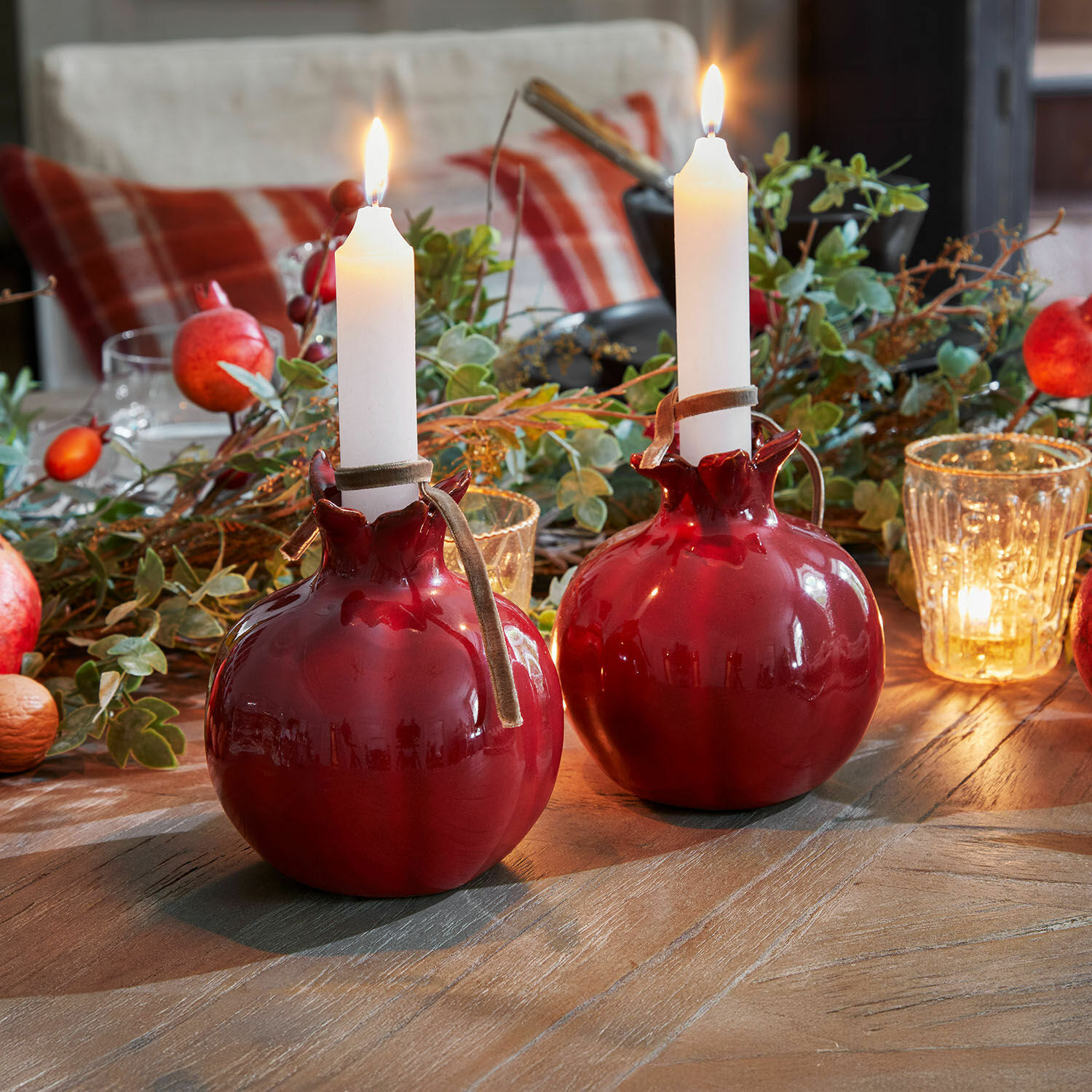 Lot de 2 bougeoirs Karidah Deux bougeoirs en céramique rouge en forme de grenade avec bougies blanches sur une table en bois décorée