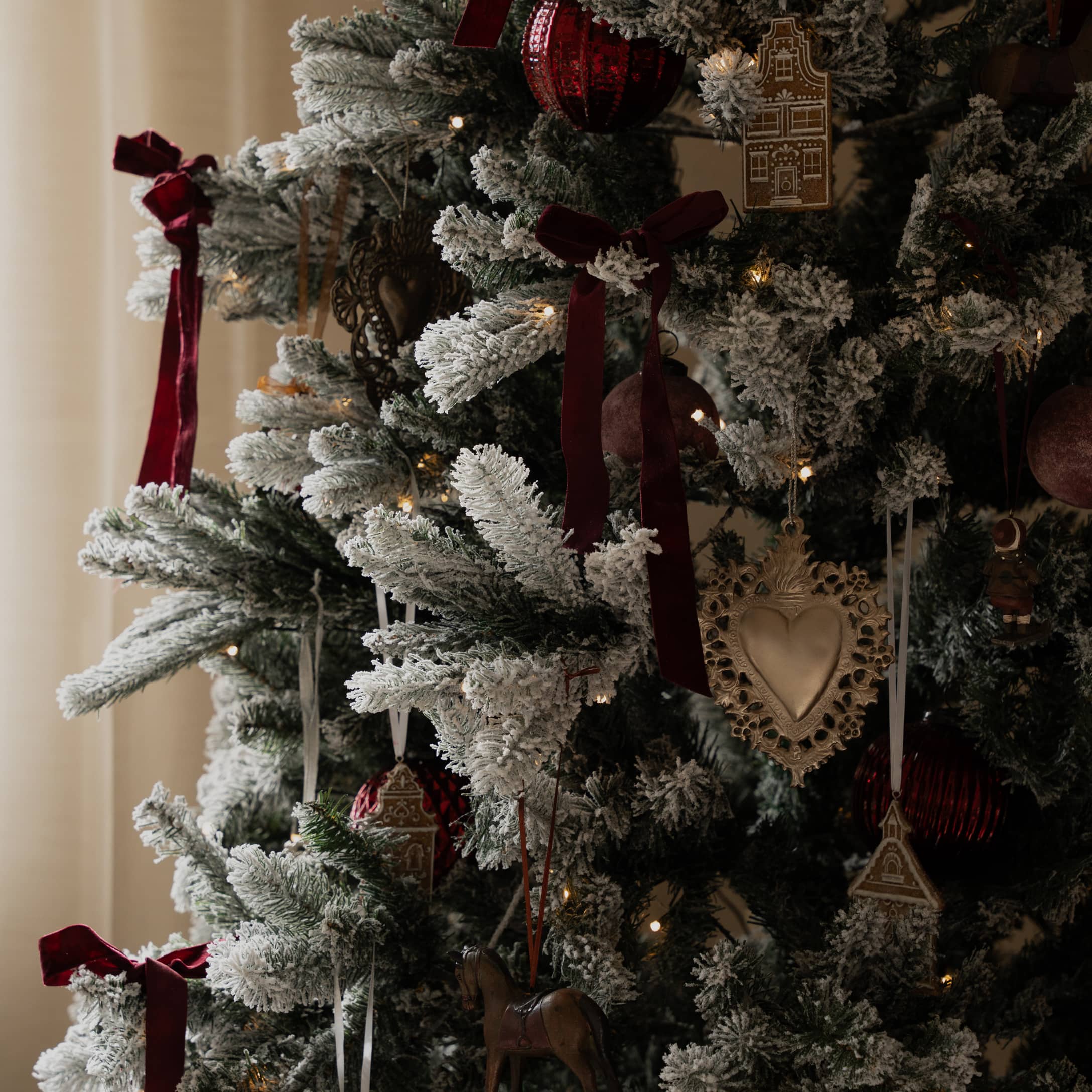 Sapin artificiel avec effet neige blanche, rubans rouges et décorations de Noël traditionnelles