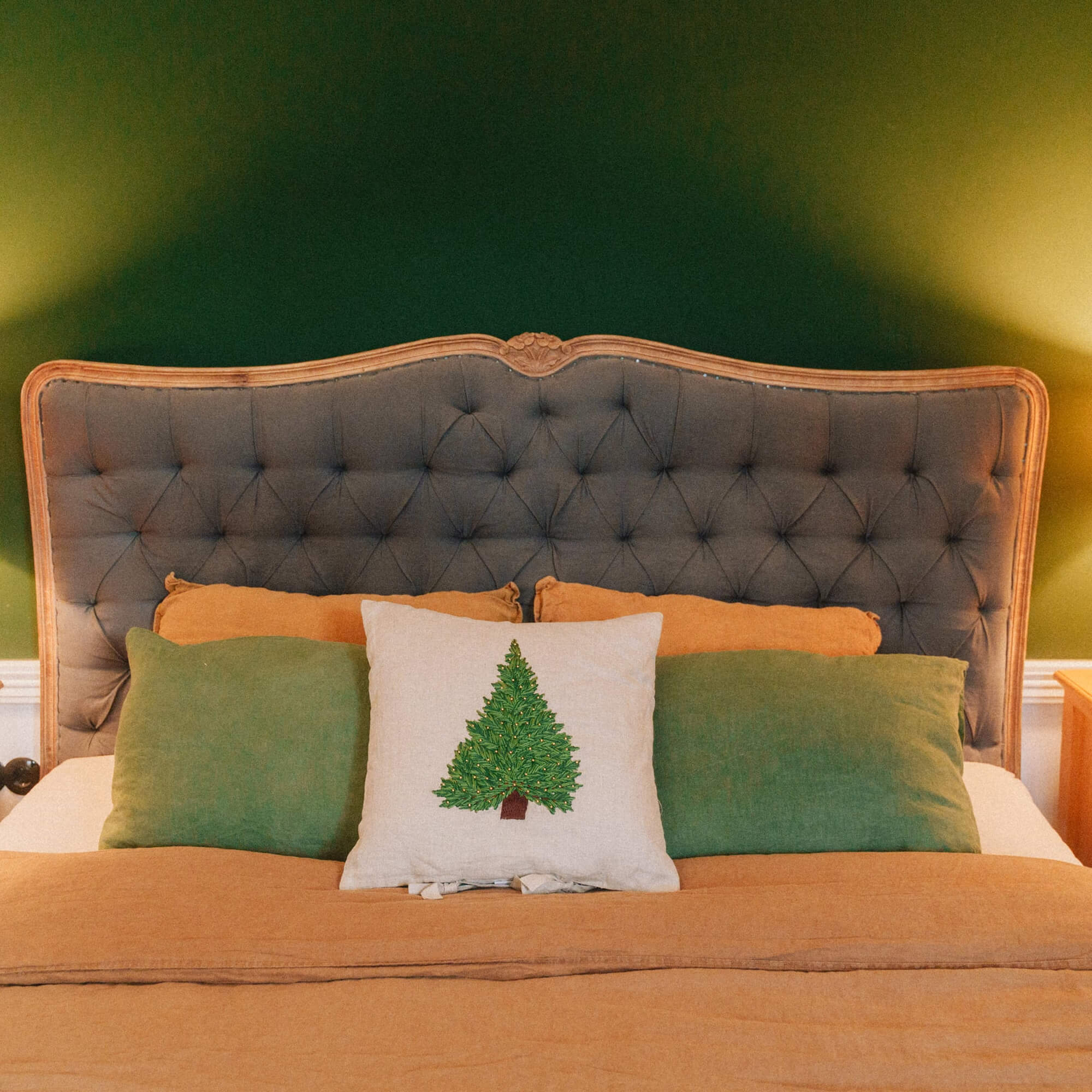 Chambre avec tête de lit grise capitonnée et coussin sapin sur une literie orange