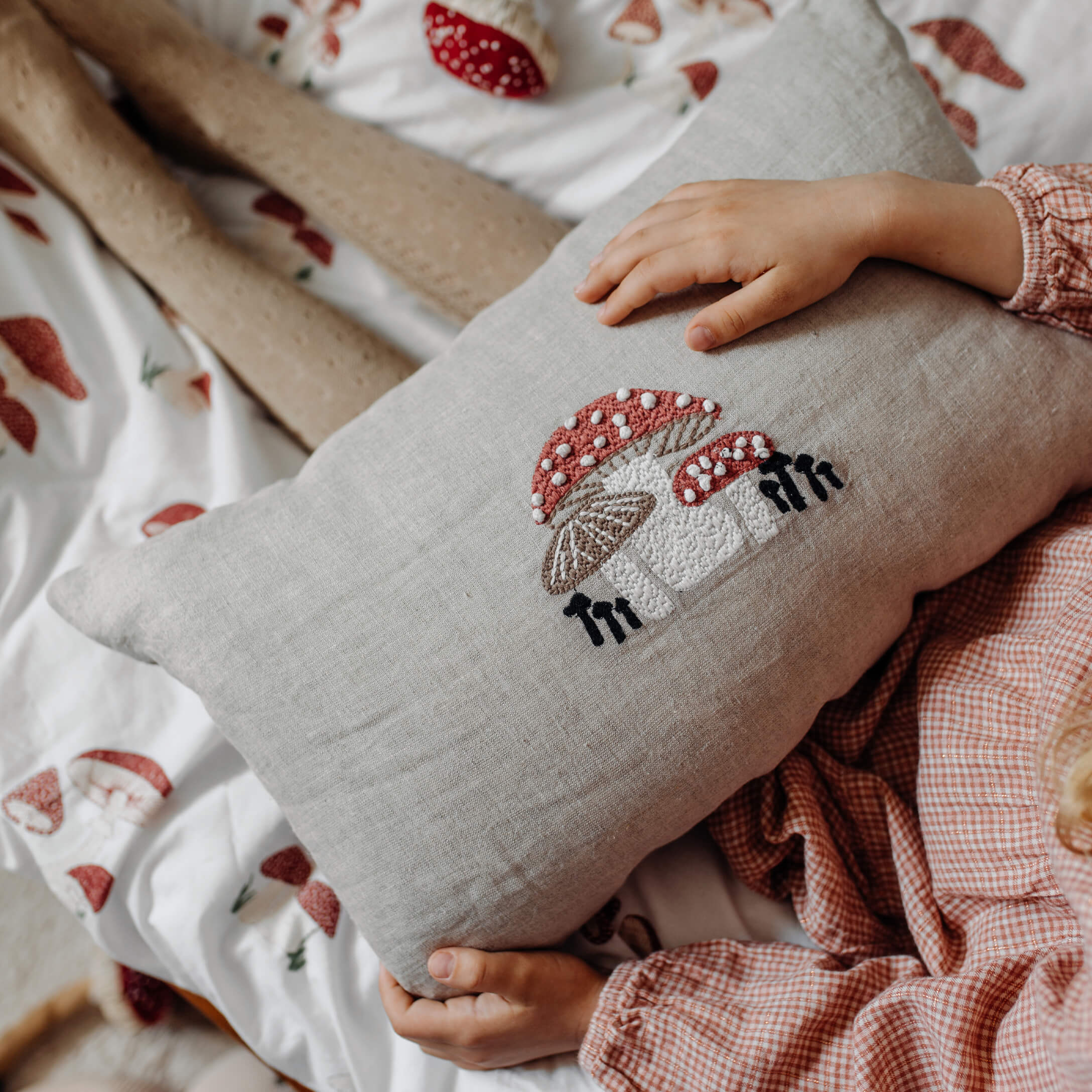 Coussin en lin avec broderie de champignons rouges et blancs sur une literie à motif champignon