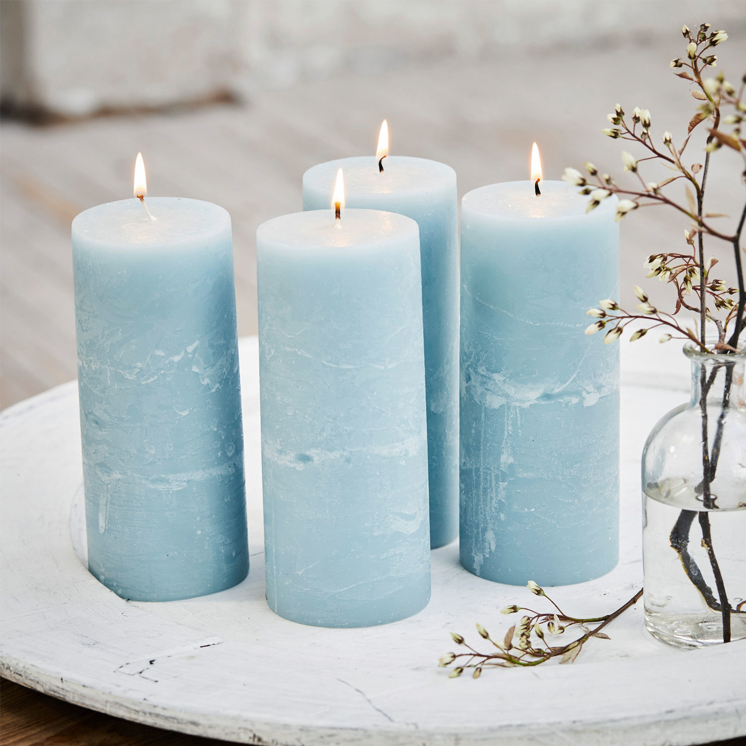 Lot de 4 bougies Homel Ensemble de quatre bougies bleues en cire sur un plateau blanc avec branche fleurie décorative