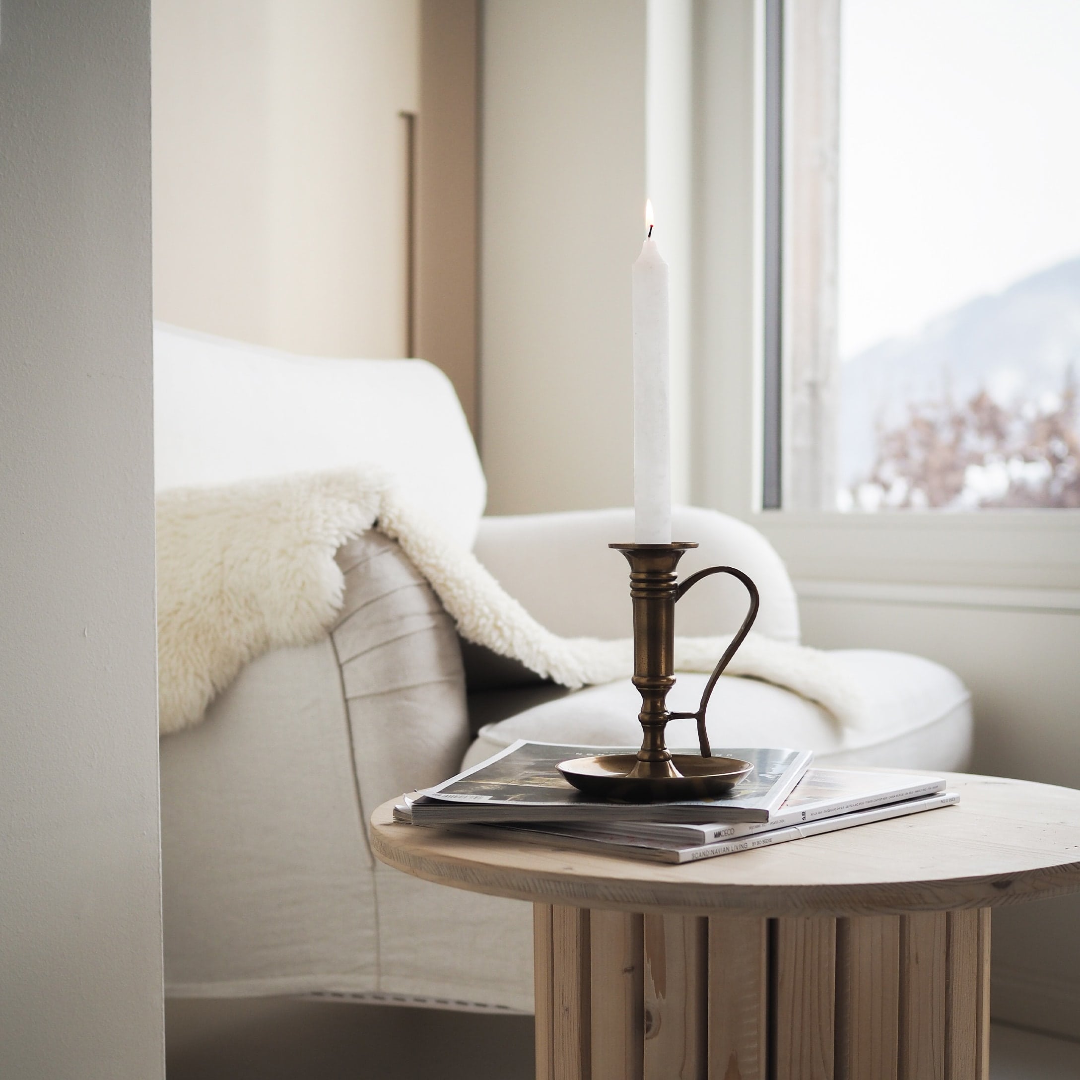Chandelier en laiton avec bougie blanche sur table en bois près d'un canapé blanc et d'une couverture