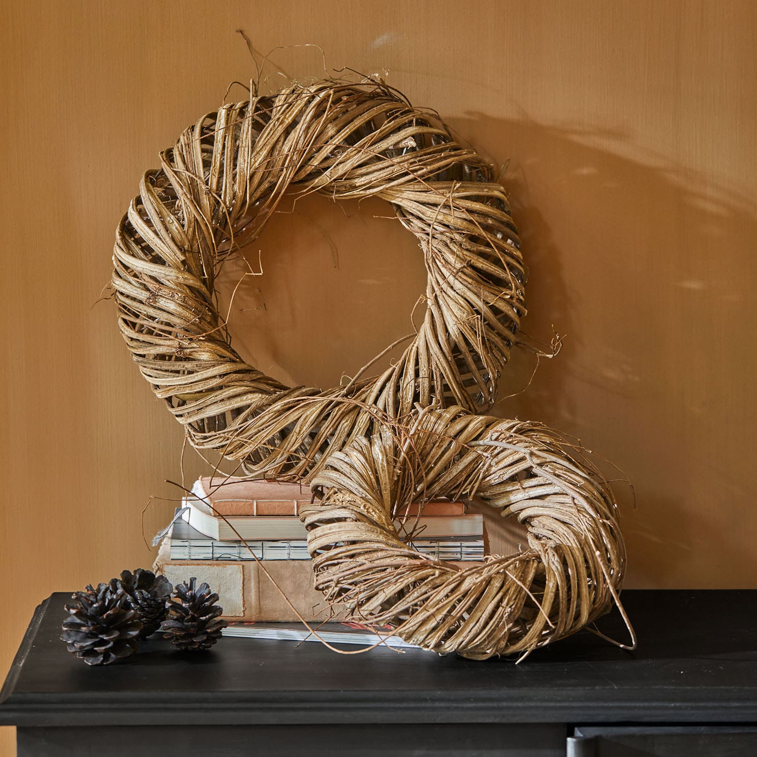 Couronnes décoratives en osier naturel brun posées sur une surface noire avec des pommes de pin décoratives