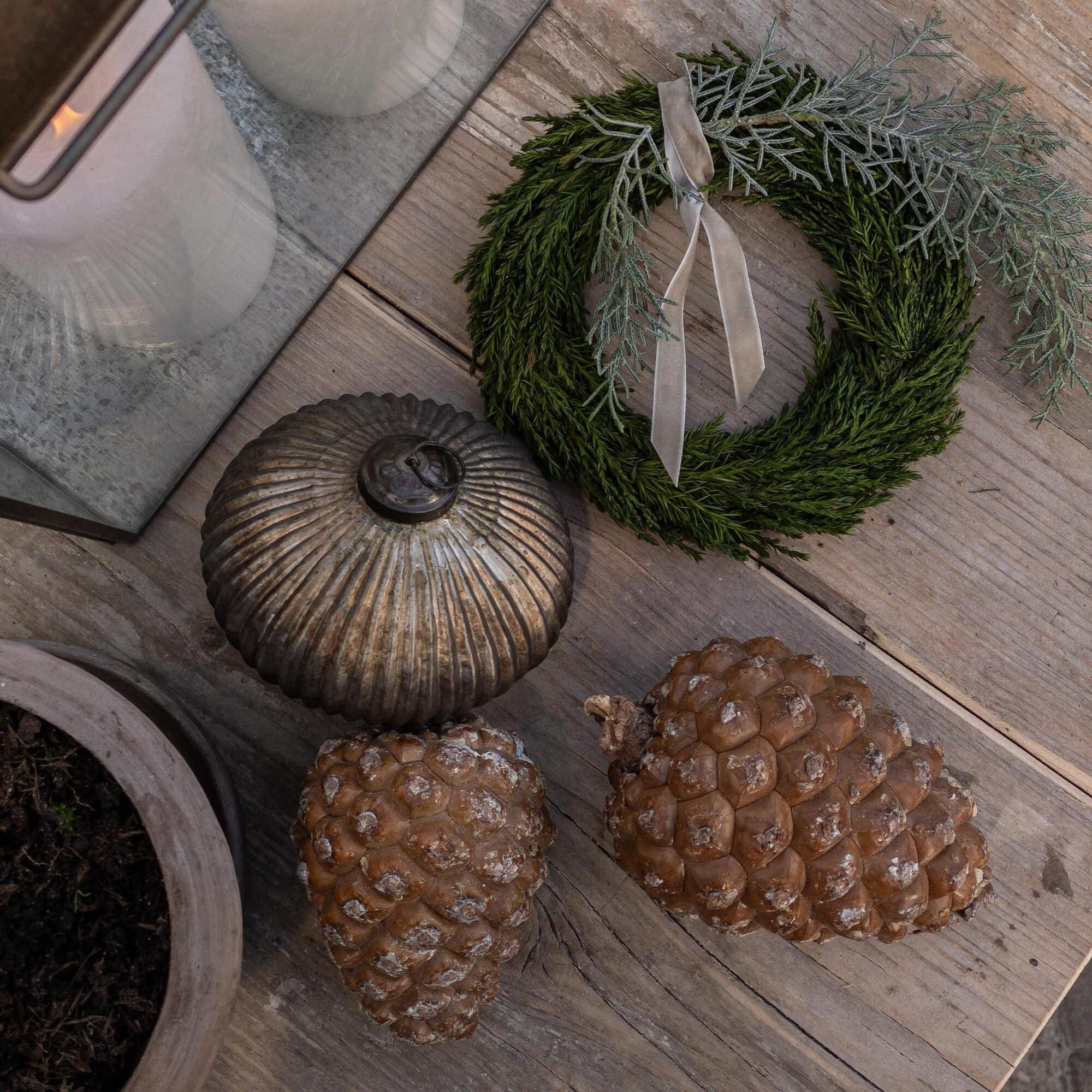 Couronne décorative en branches vertes avec ruban gris et pommes de pin naturelles sur table en bois