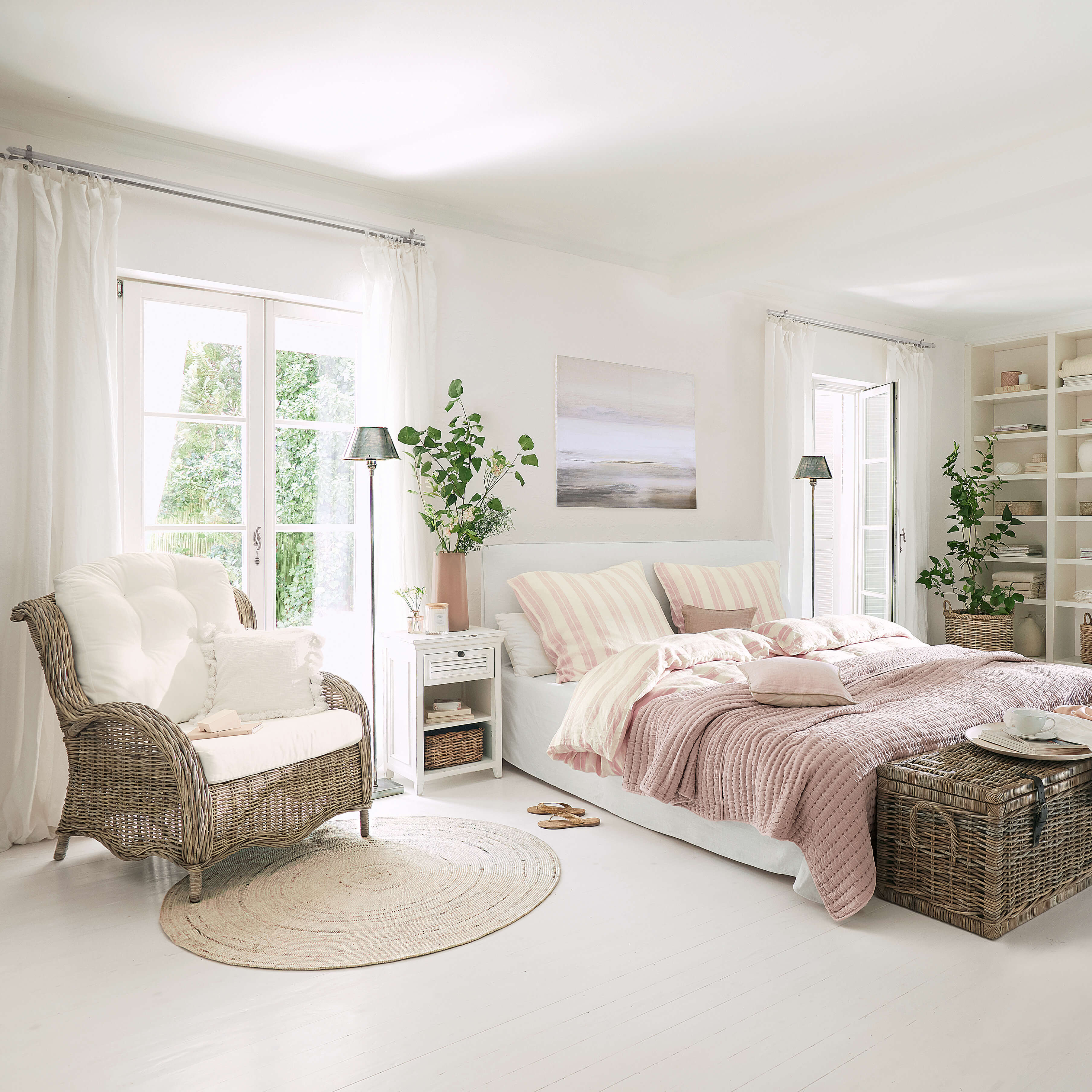 Chambre lumineuse avec lit blanc, linge de lit rose et fauteuil en osier sur sol clair