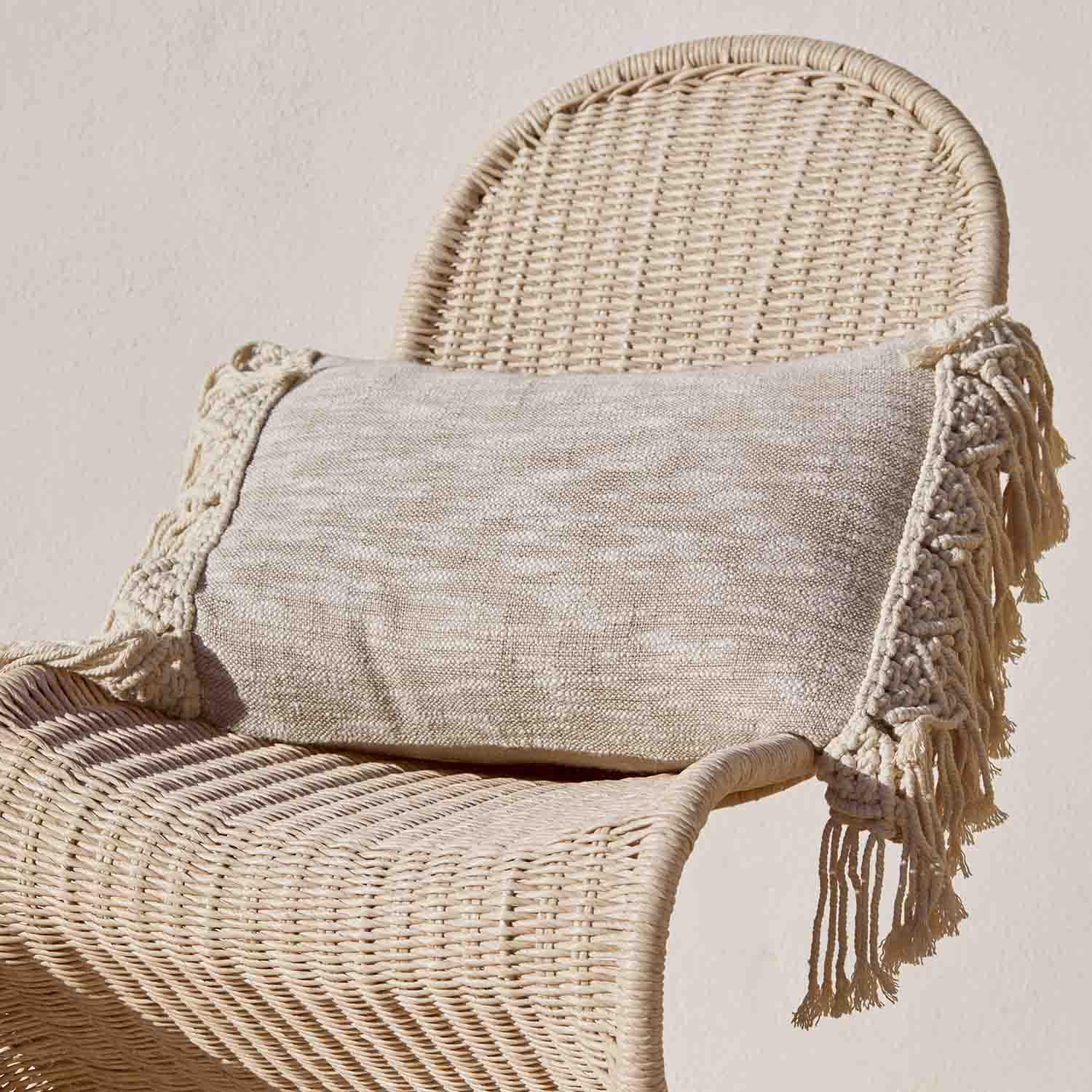 Coussin décoratif beige avec franges sur chaise en osier, tissu naturel, style bohème